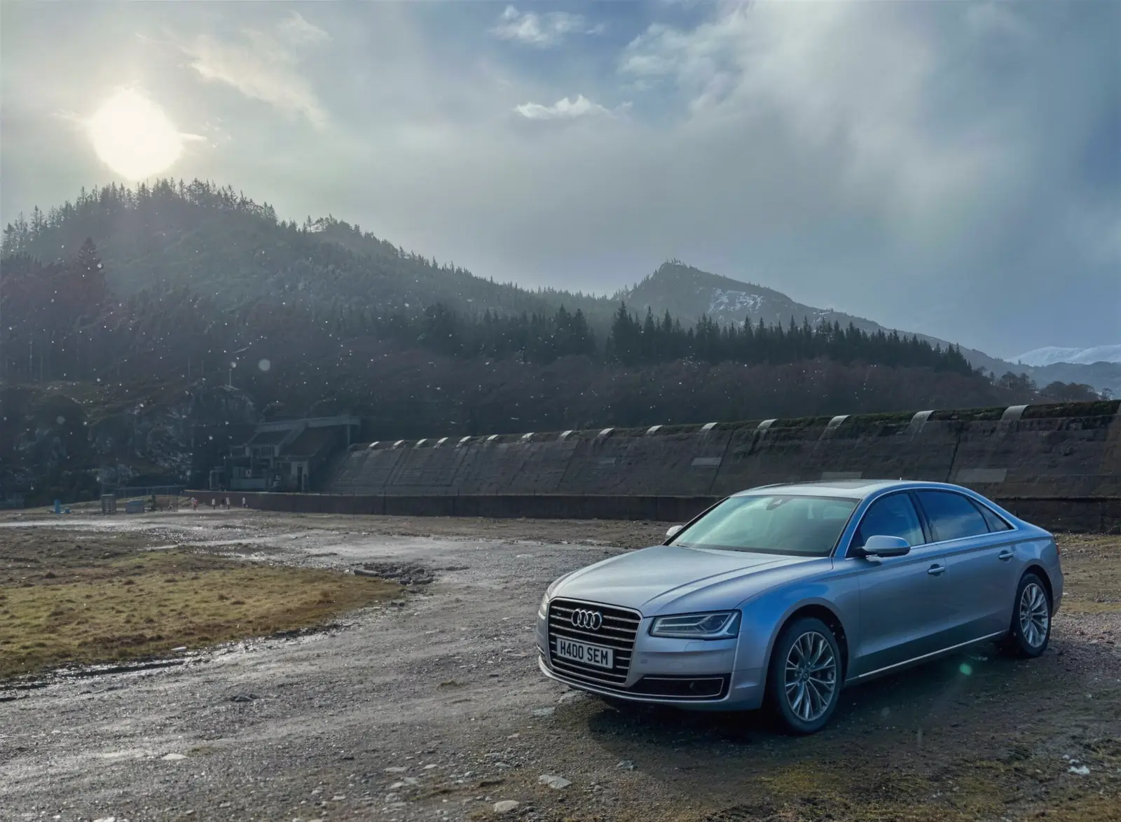 Silver Audi A8 L parked below a Highland dam under a low winter sun