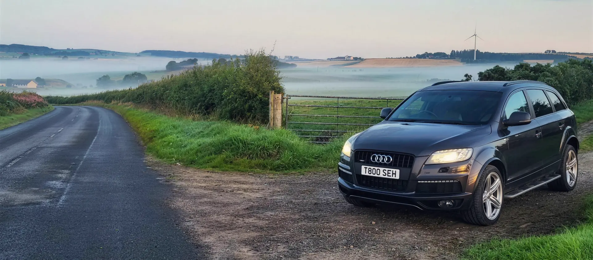 Audi Q7 parked by a country road at first light, mist lying over the fields