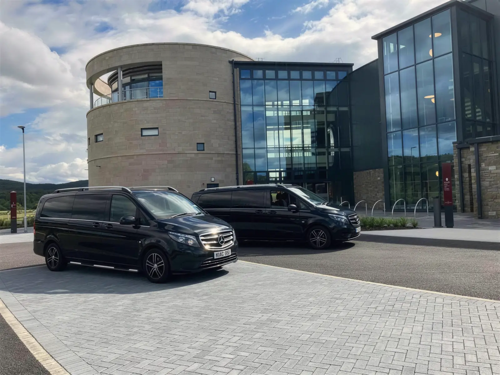 Two black Mercedes-Benz Vitos outside a modern stone and glass building